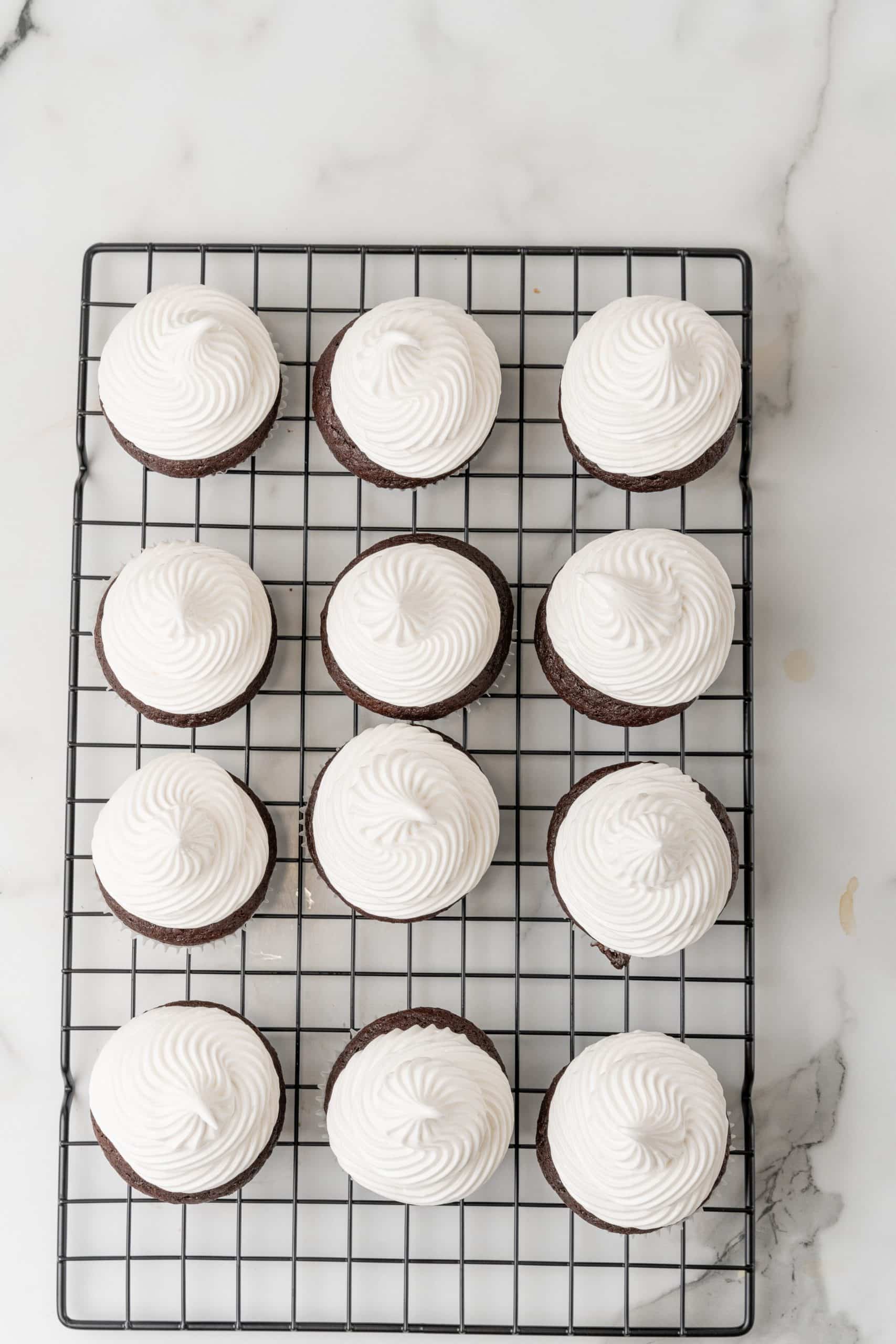 marshmallow frosting topped chocolate cupcakes on a metal cooling rack