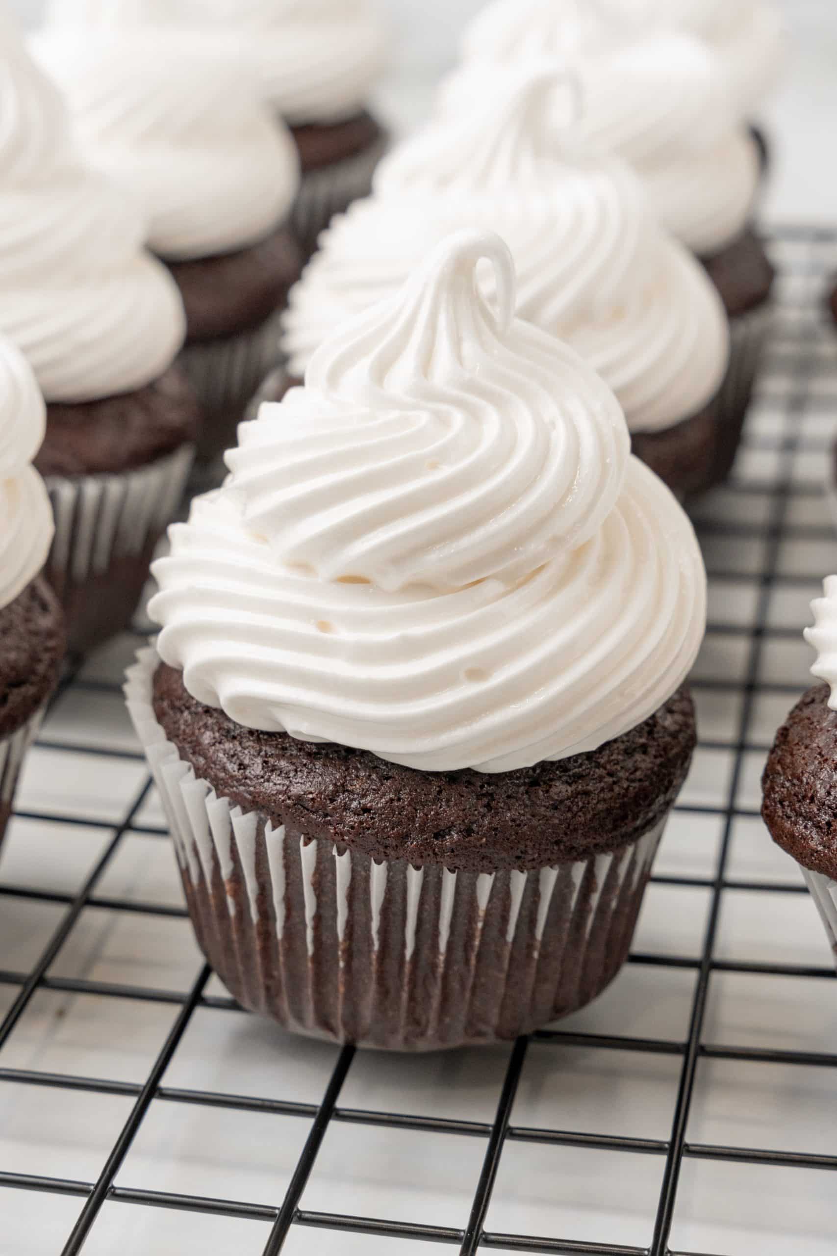 marshmallow frosting topped chocolate cupcakes on a metal cooling rack
