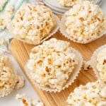 marshmallow popcorn balls in white cupcake liners on a wooden cutting board