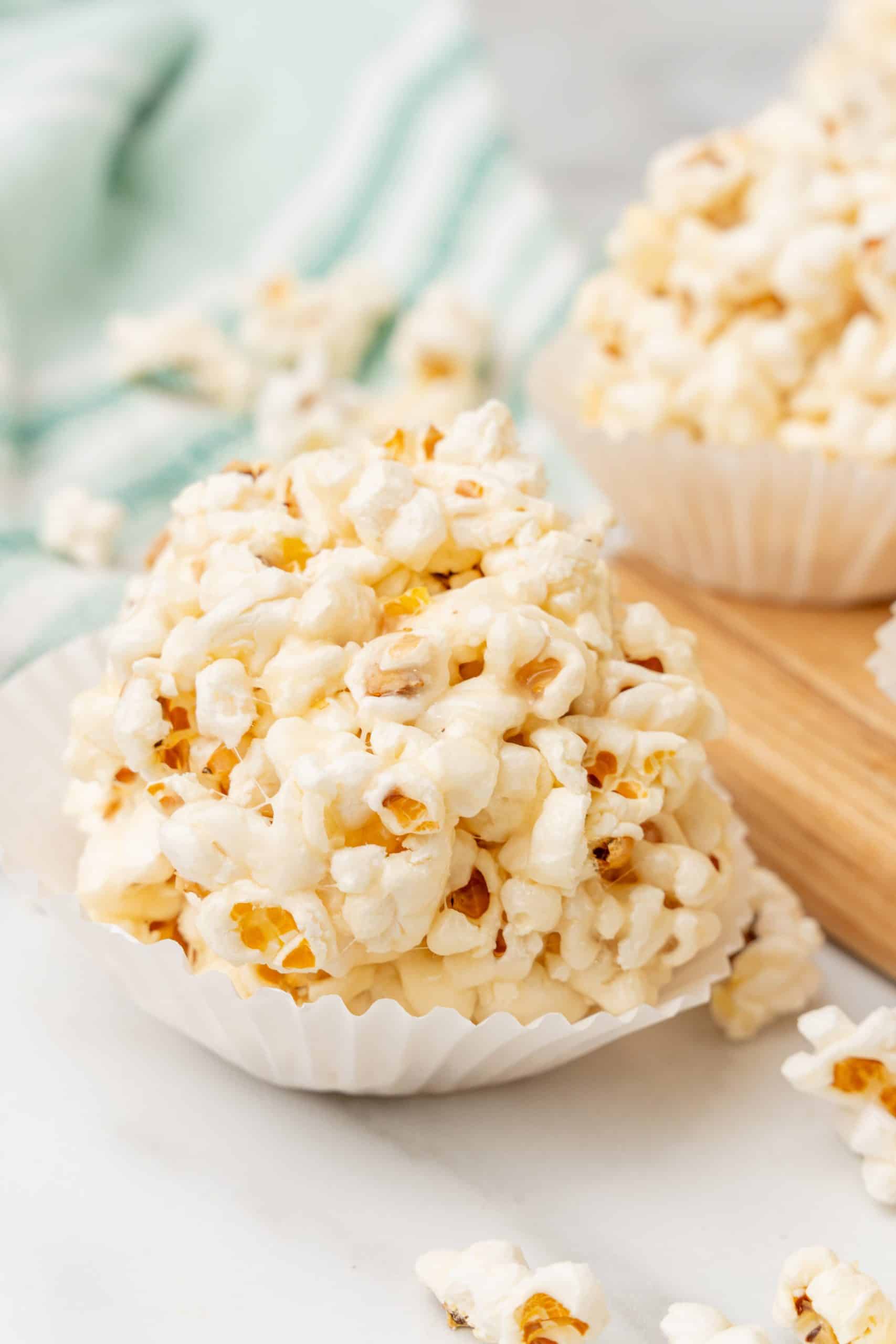 marshmallow popcorn balls in white cupcake liners on a wooden cutting board
