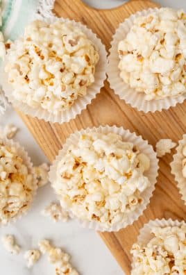 marshmallow popcorn balls in white cupcake liners on a wooden cutting board