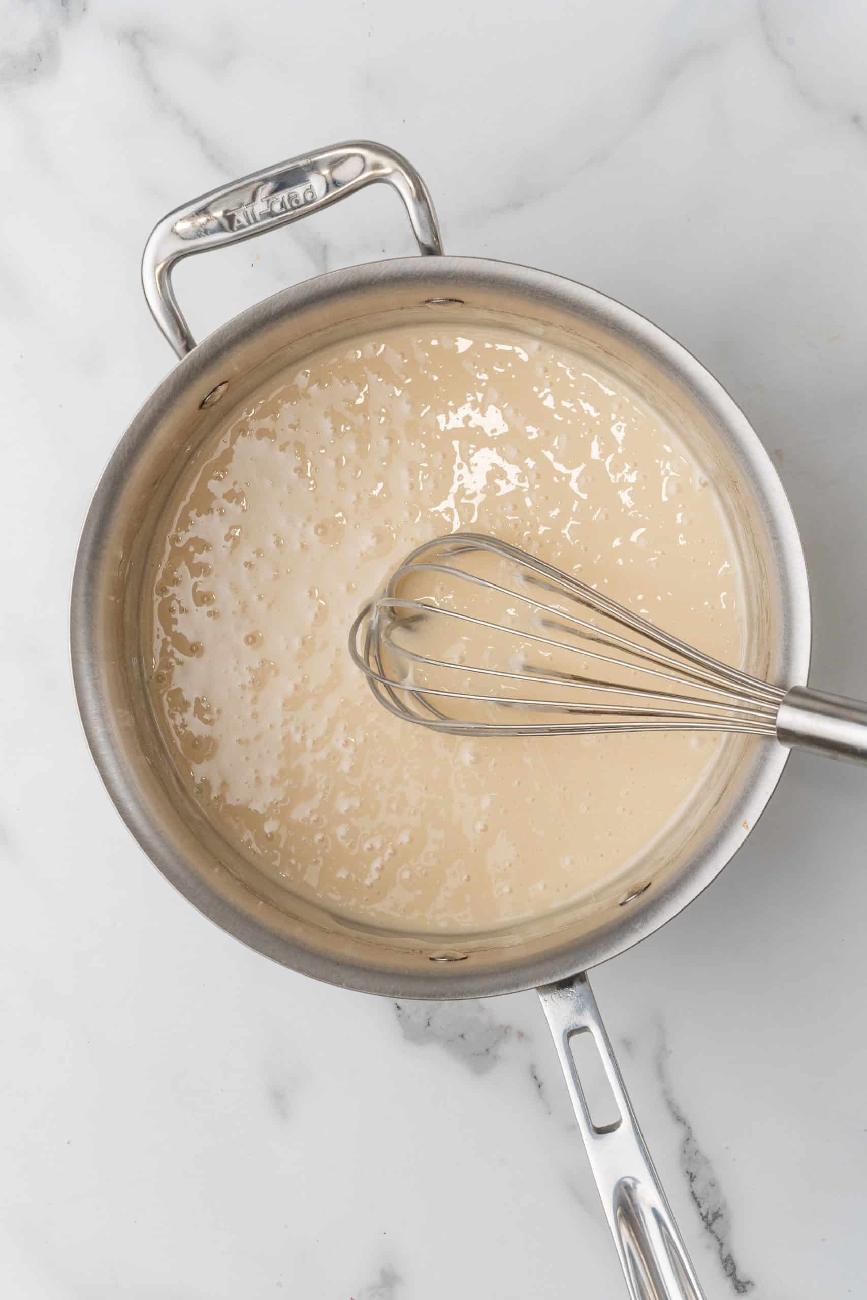 marshmallow sauce in a silver skillet with a wired whisk resting on the side