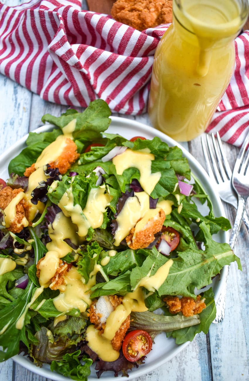 homemade honey mustard dressing recipe drizzled over a bed of lettuce on a white plate
