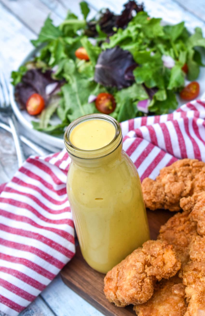 homemade honey mustard dressing recipe in a glass jar surrounded by crispy chicken tenders