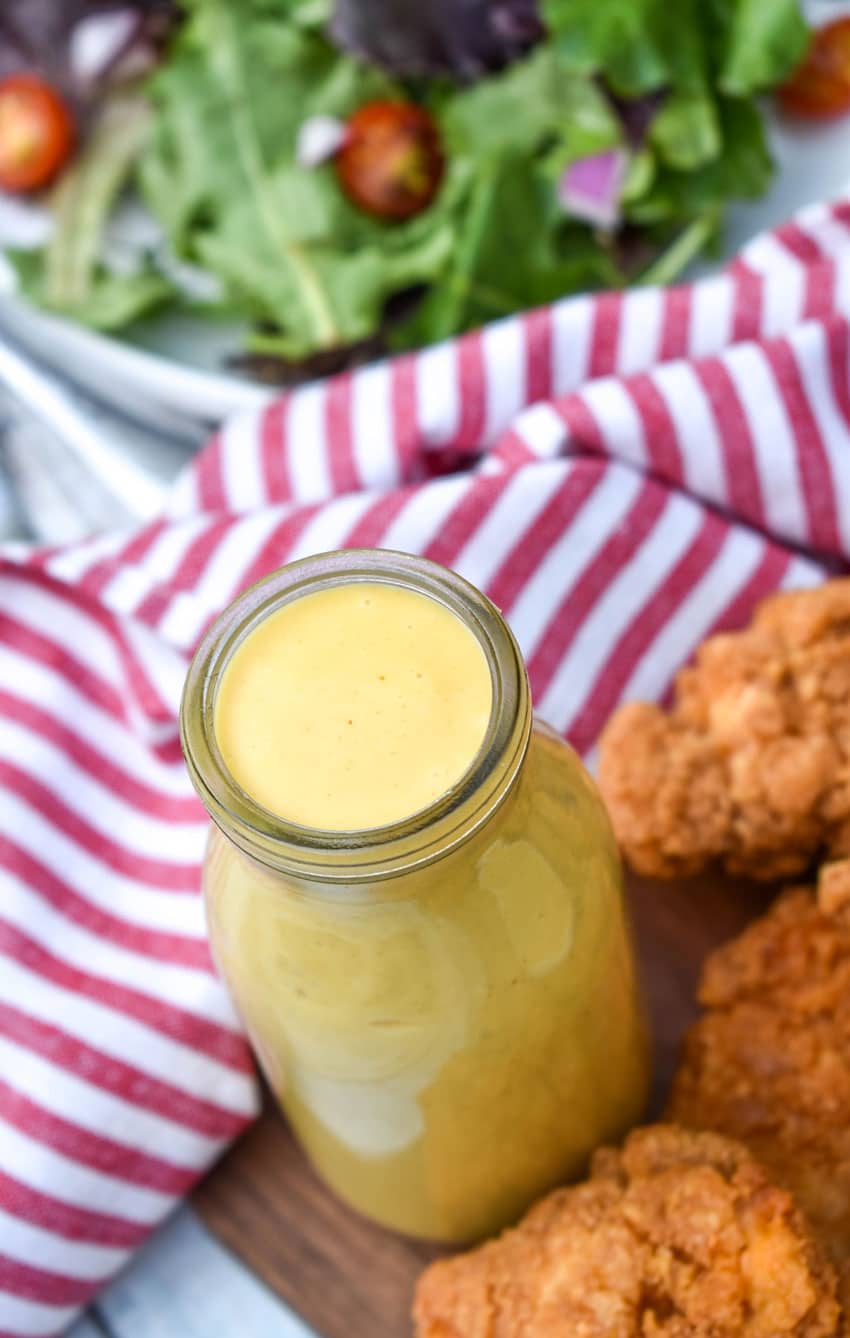 homemade honey mustard dressing recipe in a glass jar surrounded by crispy chicken tenders
