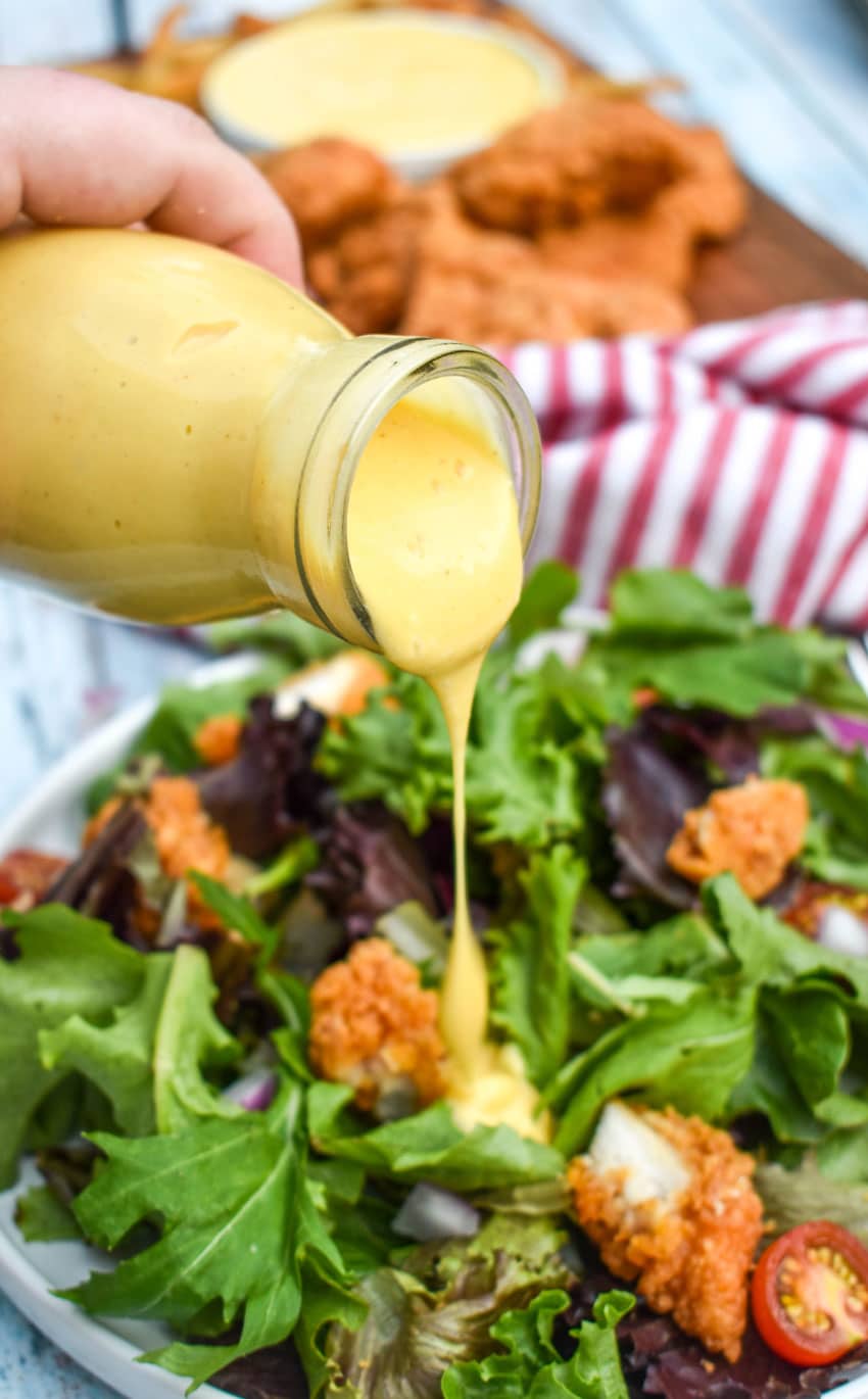 homemade honey mustard dressing being poured over a salad
