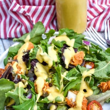 homemade honey mustard dressing recipe drizzled over a bed of lettuce on a white plate
