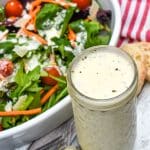 Creamy Italian dressing recipe in a small glass jar next to a tossed garden salad in a white bowl