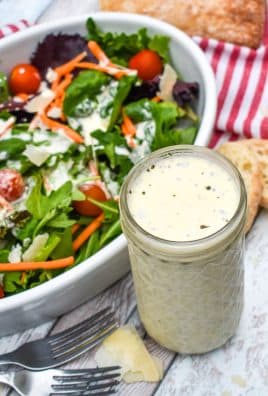 Creamy Italian dressing recipe in a small glass jar next to a tossed garden salad in a white bowl