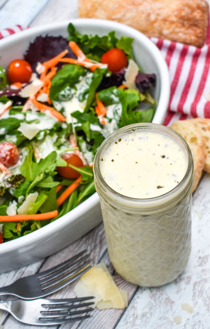 Creamy Italian dressing recipe in a small glass jar next to a tossed garden salad in a white bowl