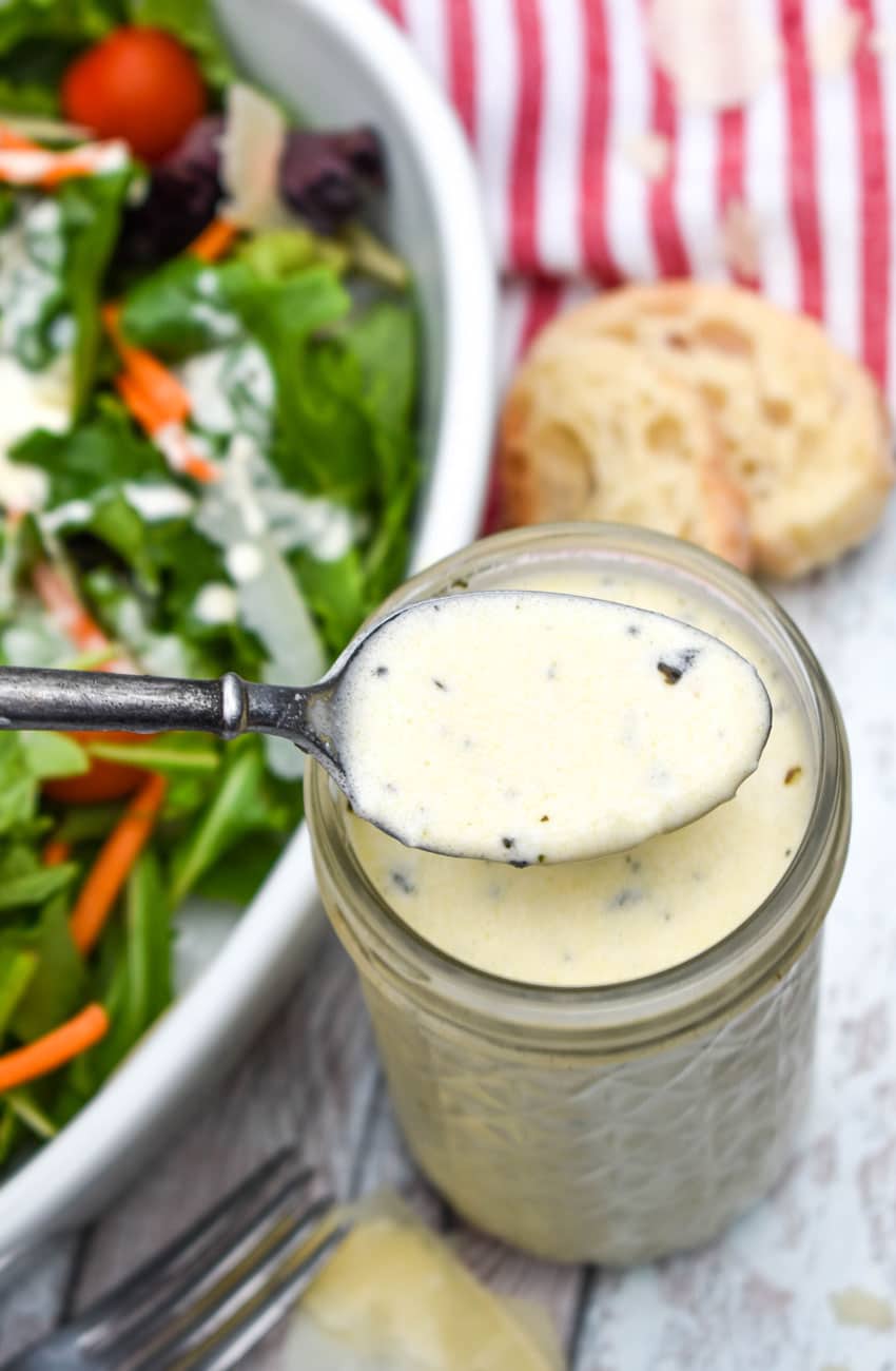 a spoon scooping creamy homemade Italian dressing out of a small glass jar