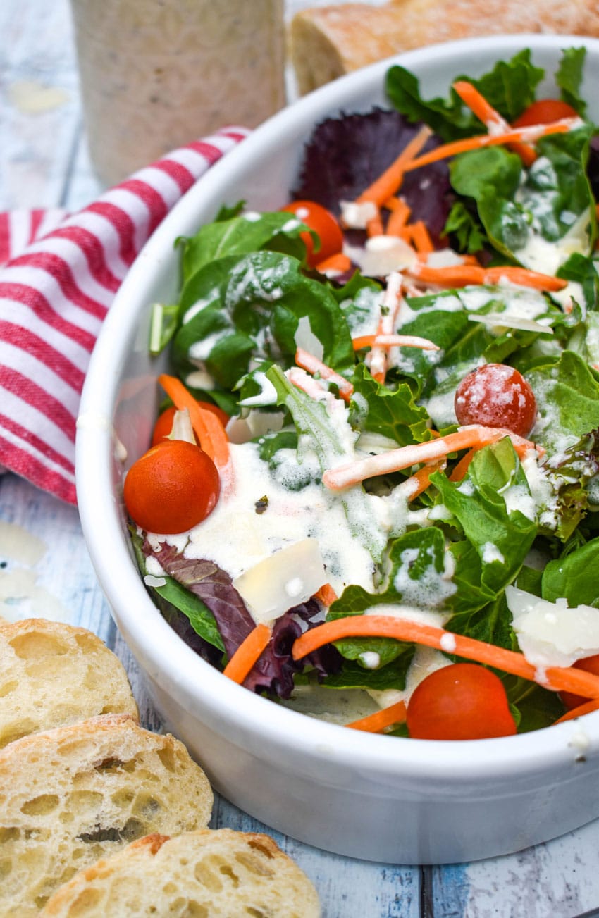 a garden salad tossed with creamy Italian dressing in a white serving bowl