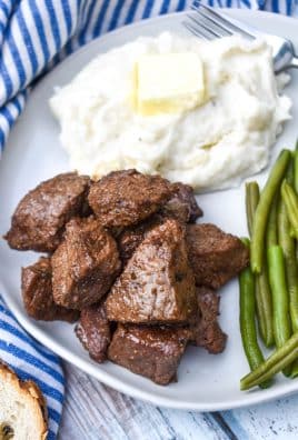 garlic butter steak bites on a white plate next to mashed potatoes and sauteed green beans