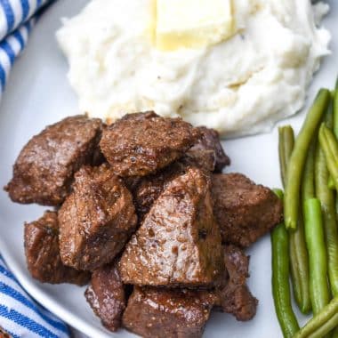 garlic butter steak bites on a white plate next to mashed potatoes and sauteed green beans