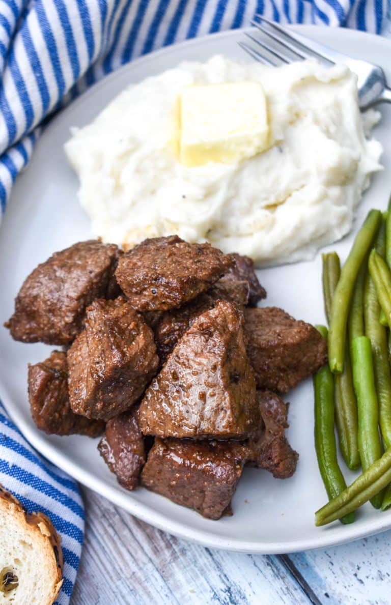 garlic butter steak bites on a white plate next to mashed potatoes and sauteed green beans