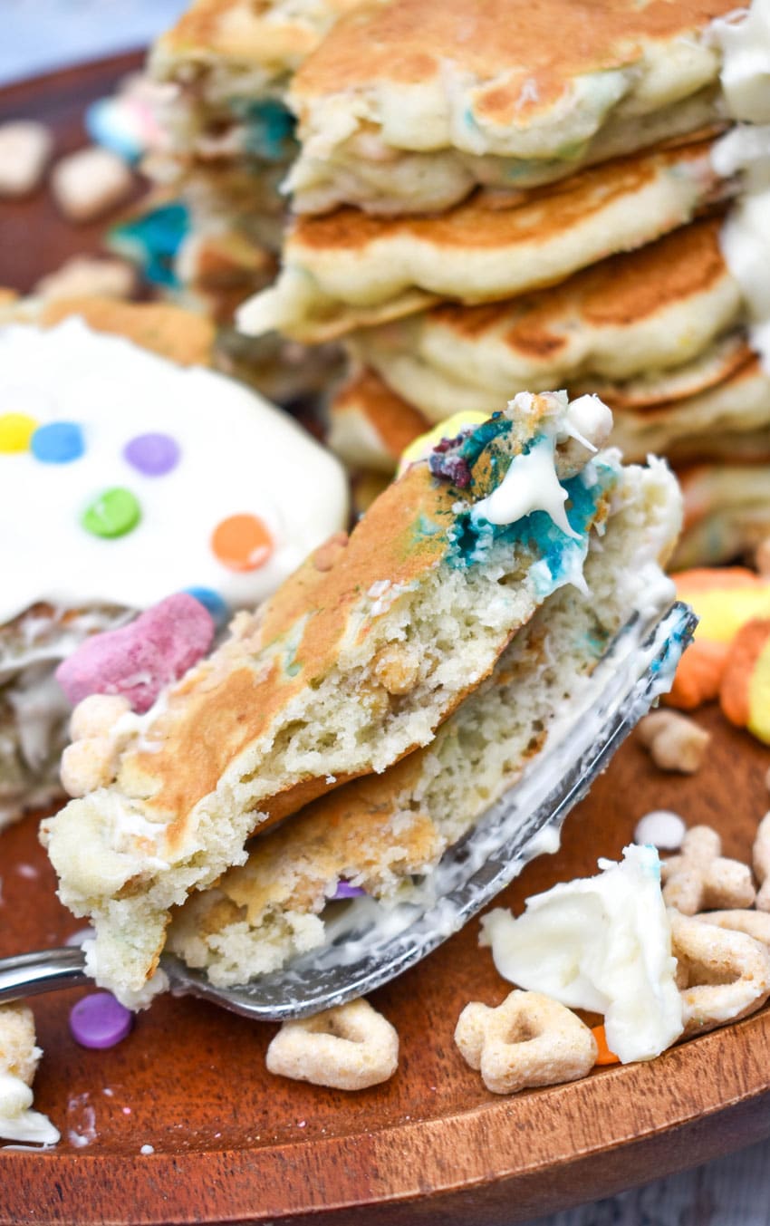 a silver fork resting on a wooden cutting board holding slices of lucky charms pancakes