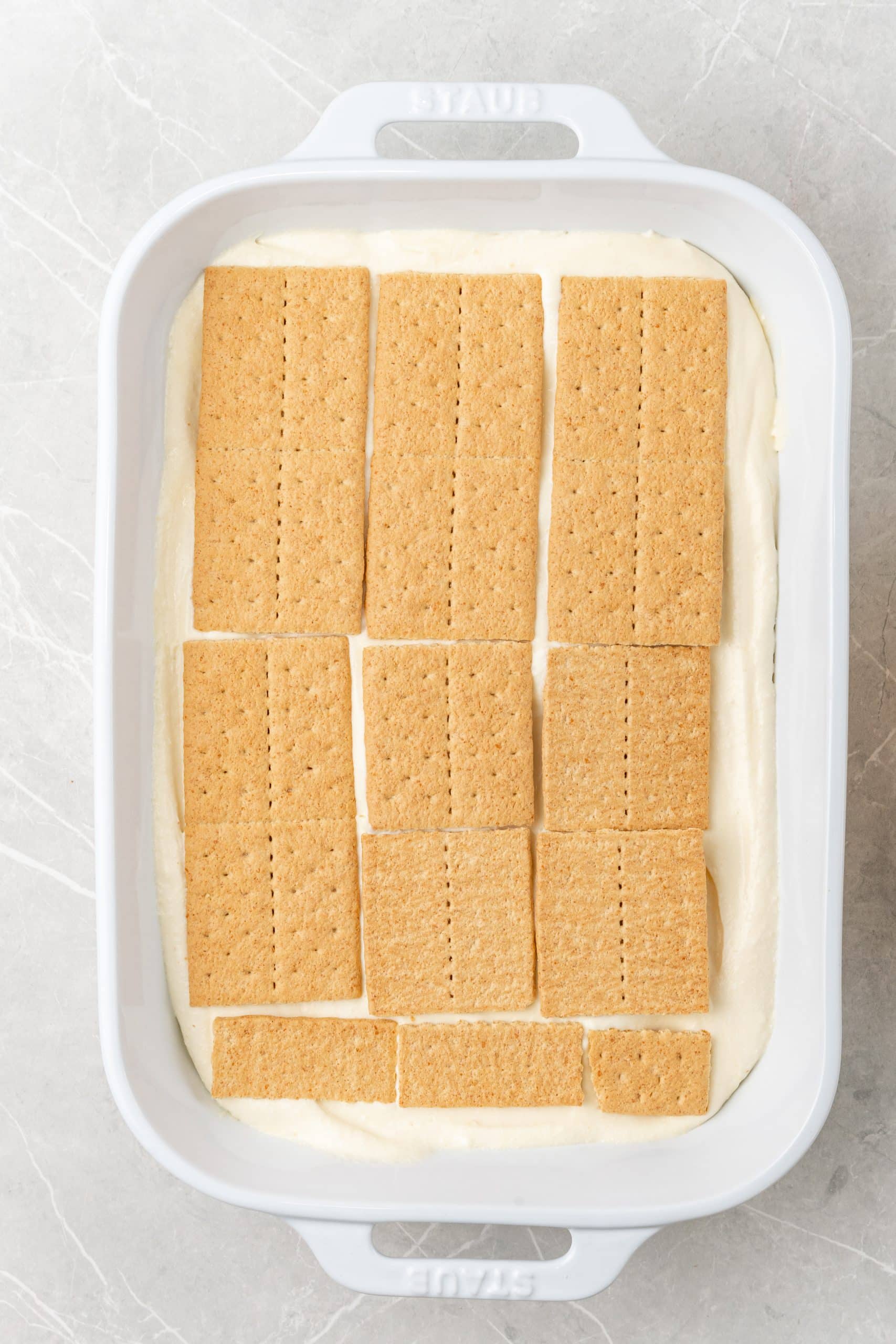 a layer of graham crackers on top of vanilla pudding in a white baking dish