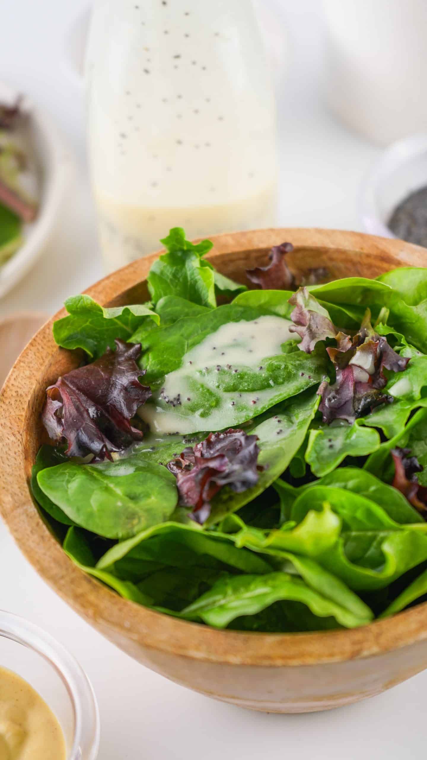 creamy poppy seed dressing on salad greens in a wooden bowl
