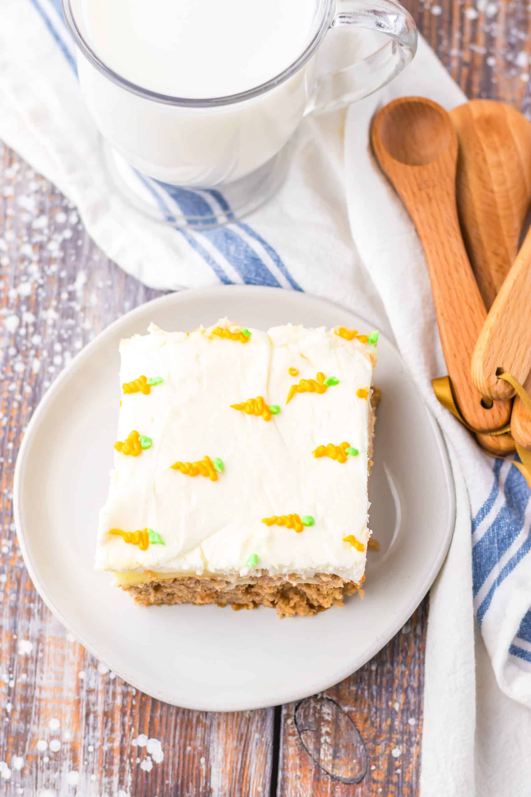 a slice of carrot cake poke cake on a small white dessert plate with a glass of milk in the background
