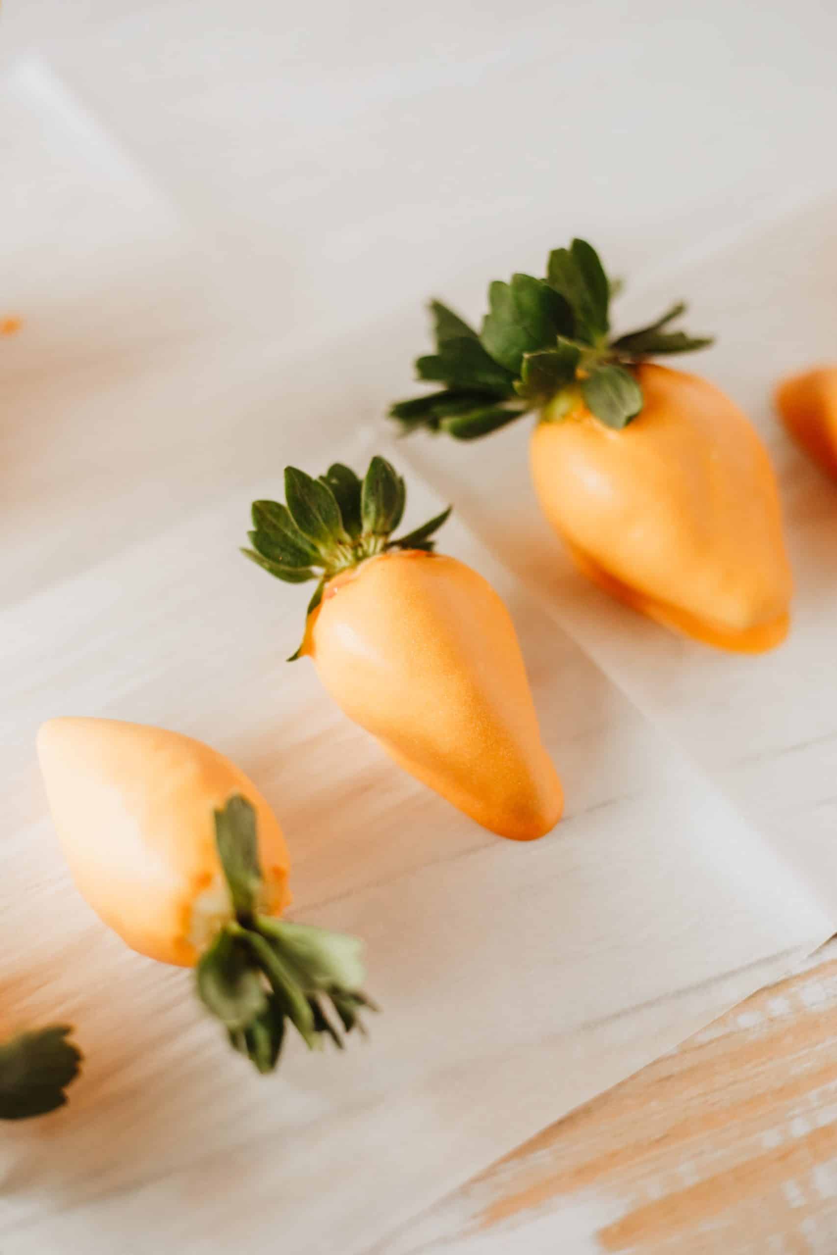 orange chocolate covered strawberries in a row on a sheet of white parchment paper