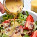 a pouring warm bacon dressing out of a small glass jar and over a bed of leafy greens