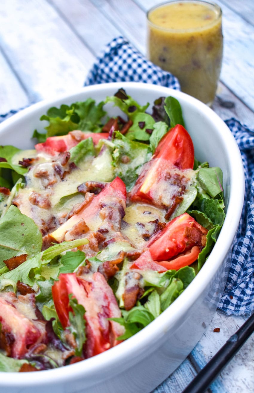 warm bacon vinaigrette dressing over salad greens in a white serving bowl