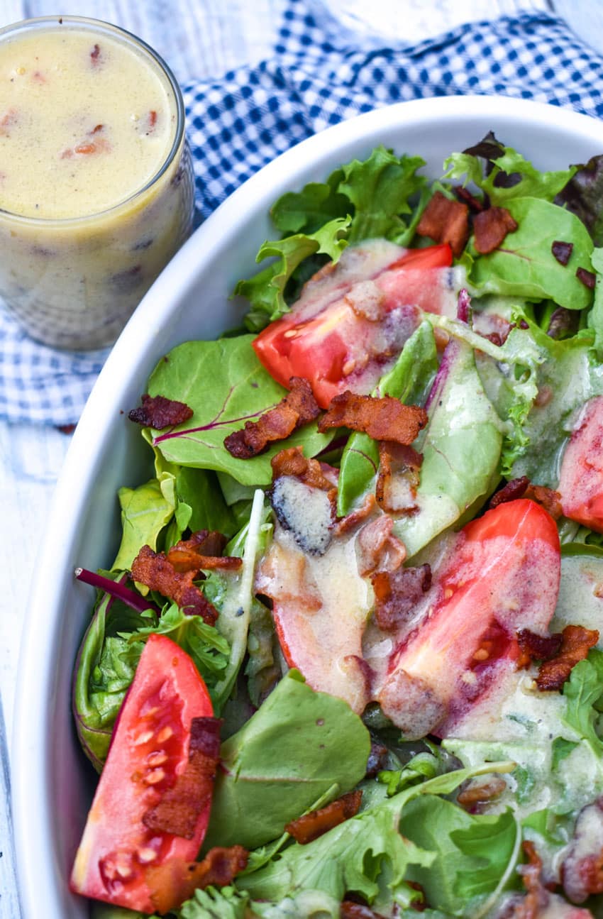 warm bacon vinaigrette dressing over salad greens in a white serving bowl