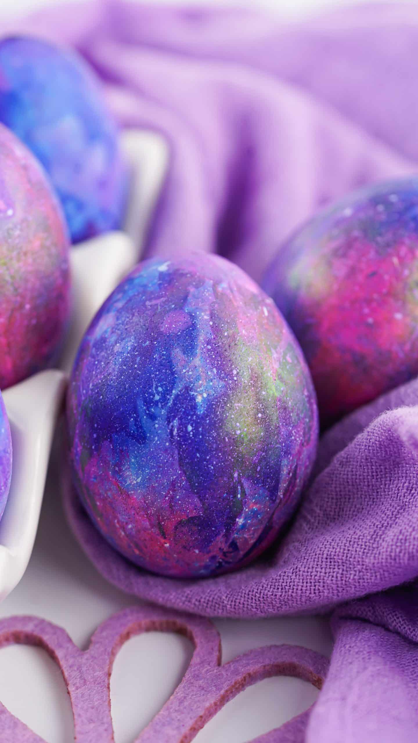 a dyed easter galaxy egg resting against the edge of a white egg holder on a purple cloth