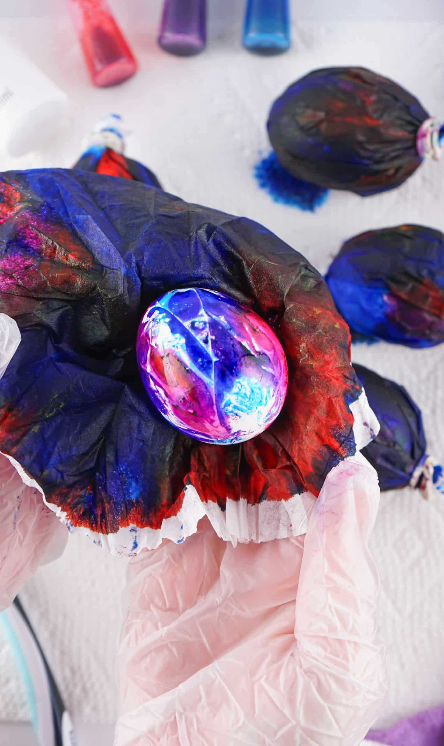a dyed easter galaxy egg being unwrapped from a food coloring soaked coffee filter