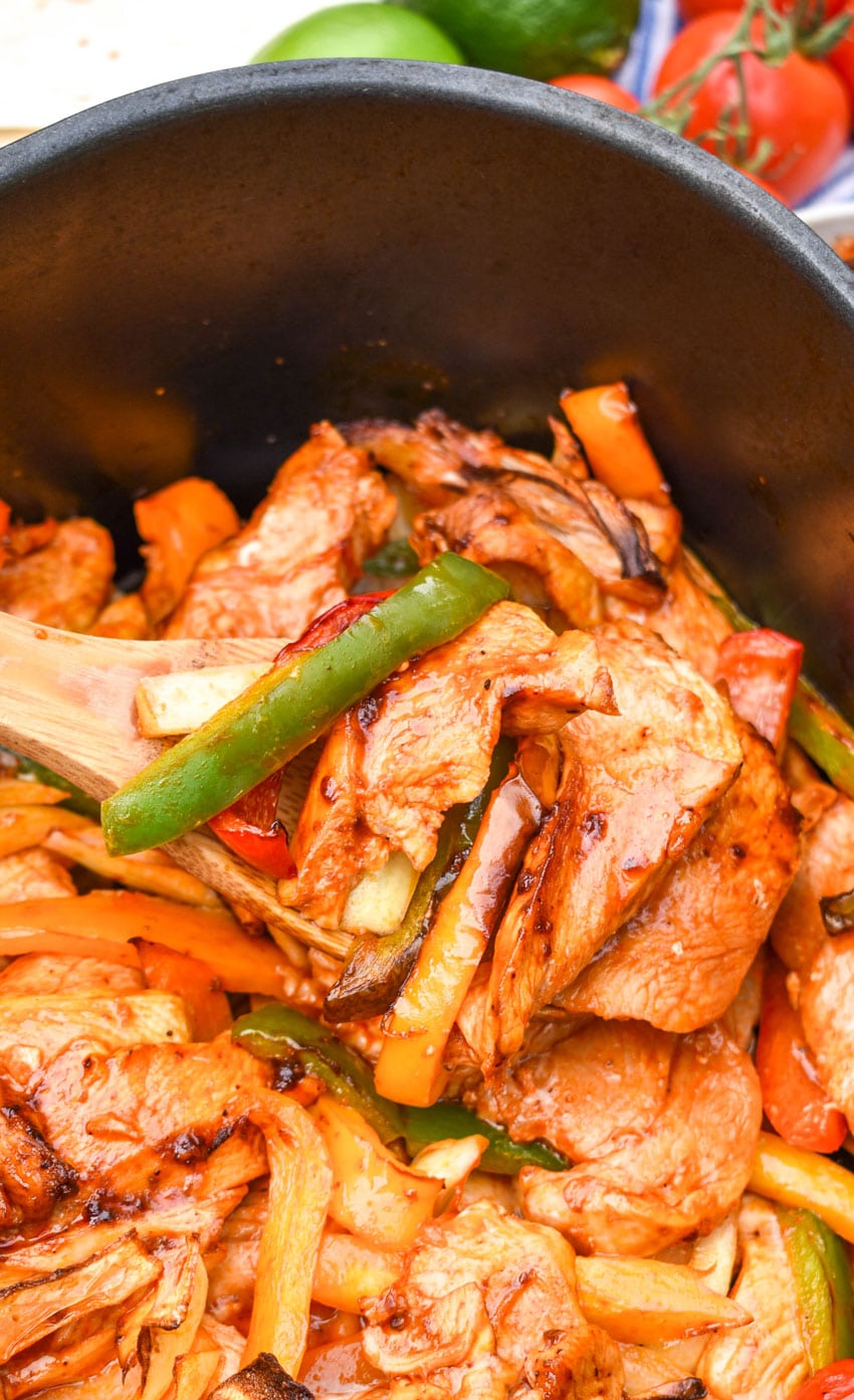 a wooden spoon scooping fajita chicken with peppers and onions out of the basket of an air fryer