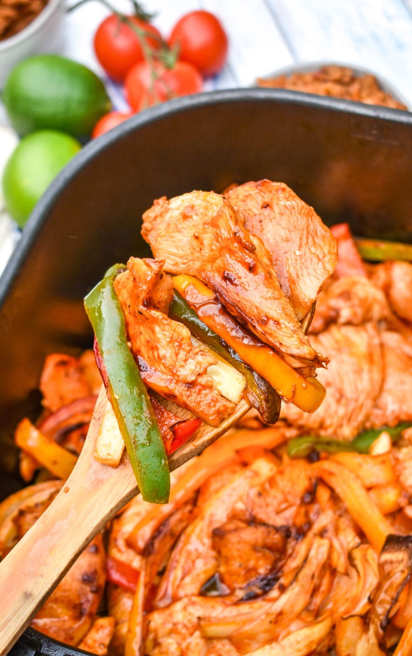 a wooden spoon scooping fajita chicken with peppers and onions out of the basket of an air fryer
