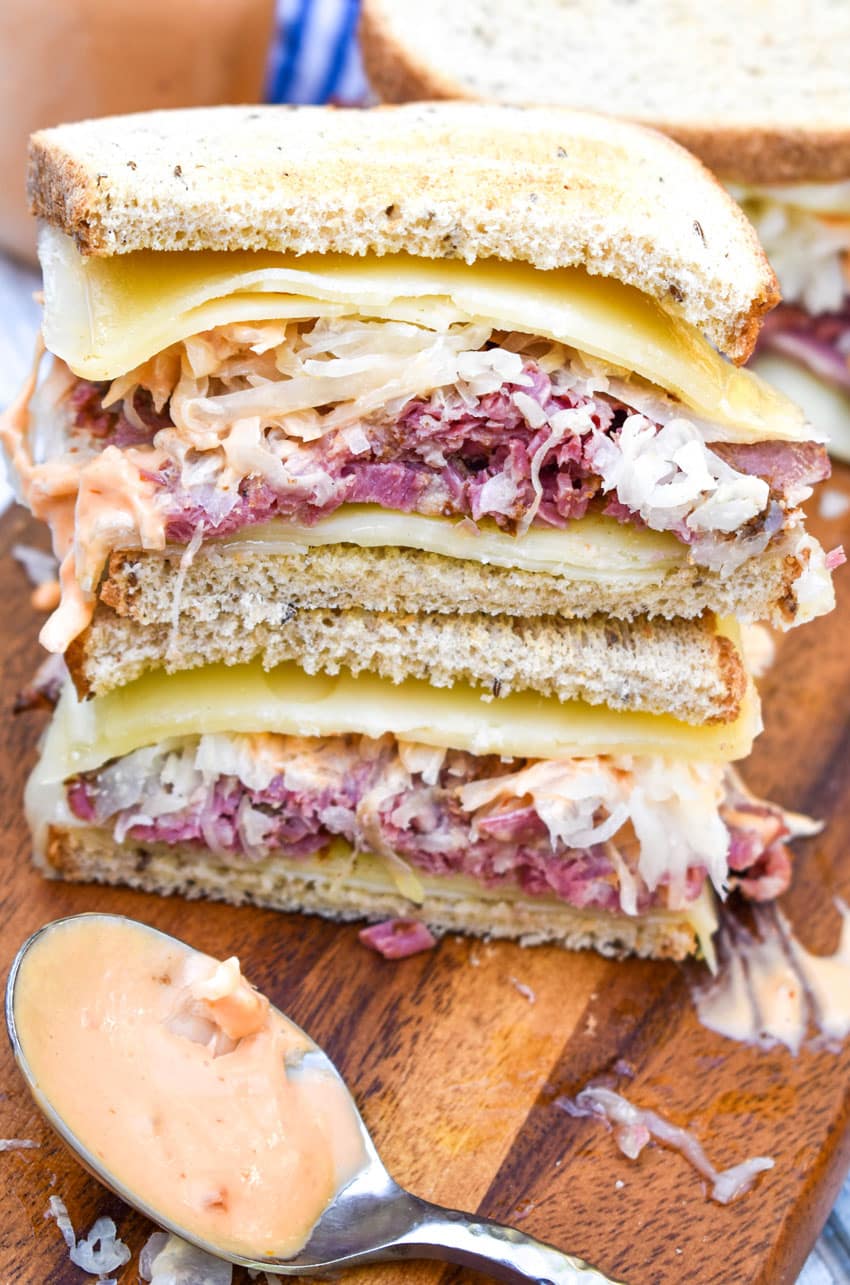 two halves of a traditional reuben sandwich stacked on top of each other on a wooden cutting board