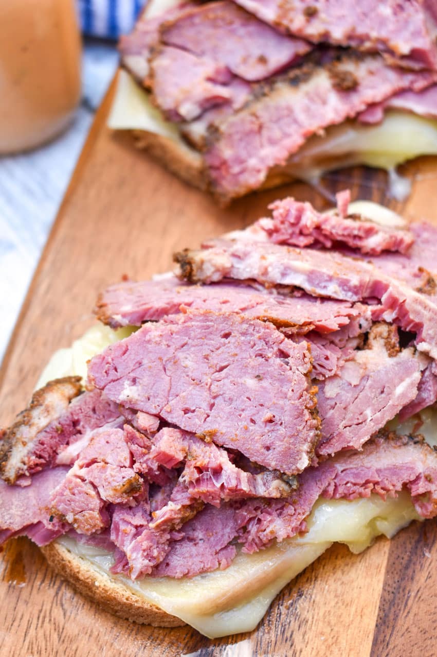 an open faced pastrami and swiss sandwich on a wooden cutting board