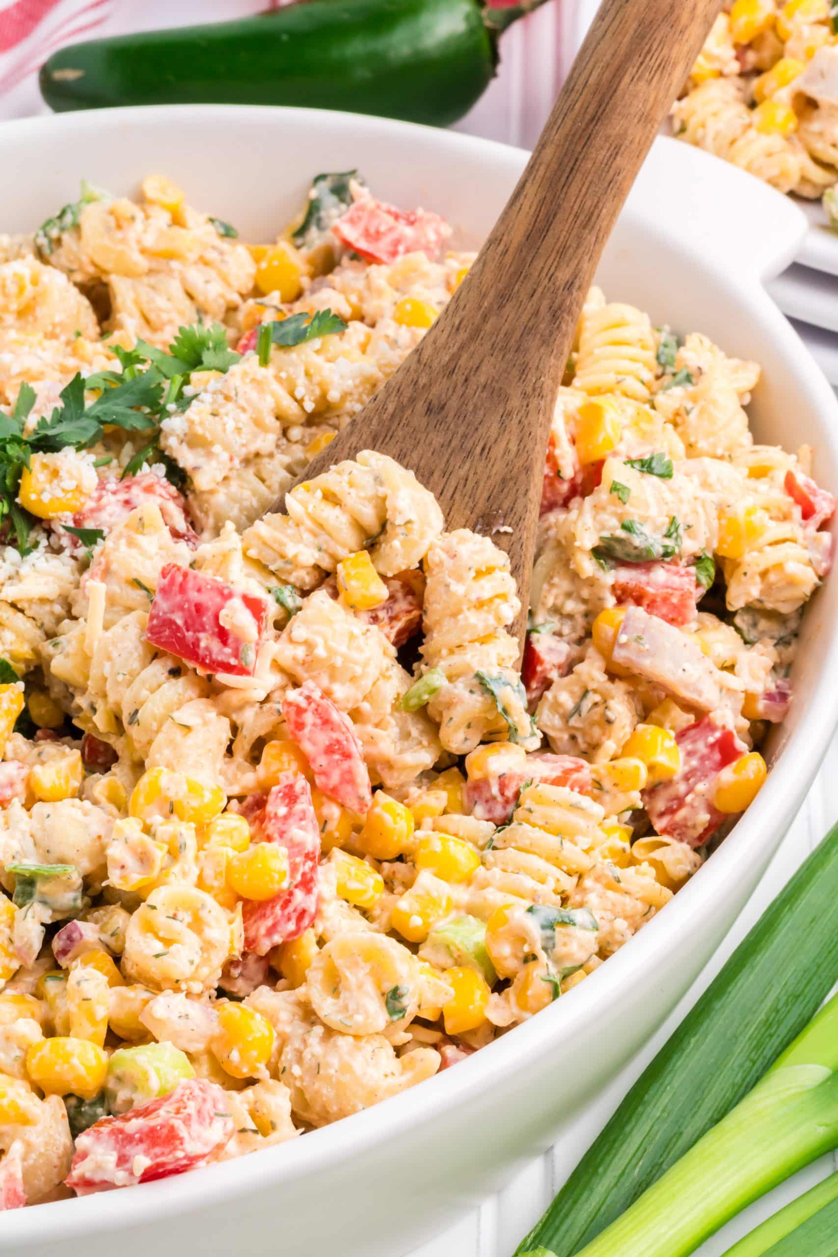 a wooden spoon scooping mexican street corn pasta salad out of a white bowl