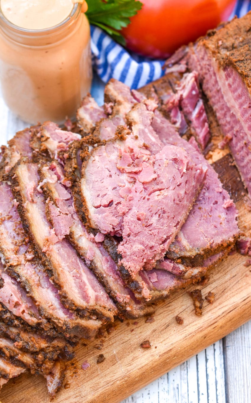 slices of a slow cooker pastrami recipe spread out in a row on a wooden cutting board
