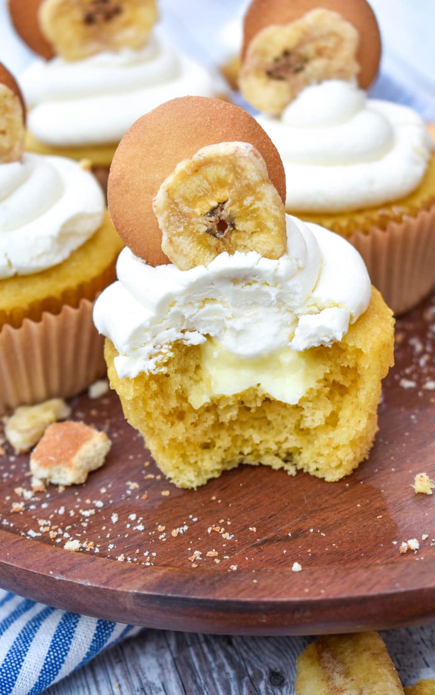 a bitten banana pudding cupcake on a wooden cake stand revealing the pudding filling in the center