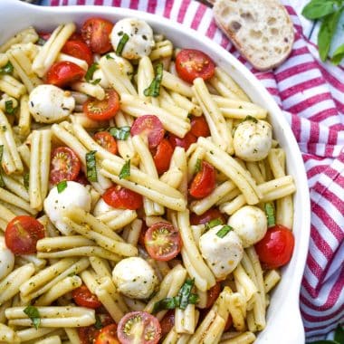 caprese pasta salad in a white serving bowl with a wooden spoon on the side