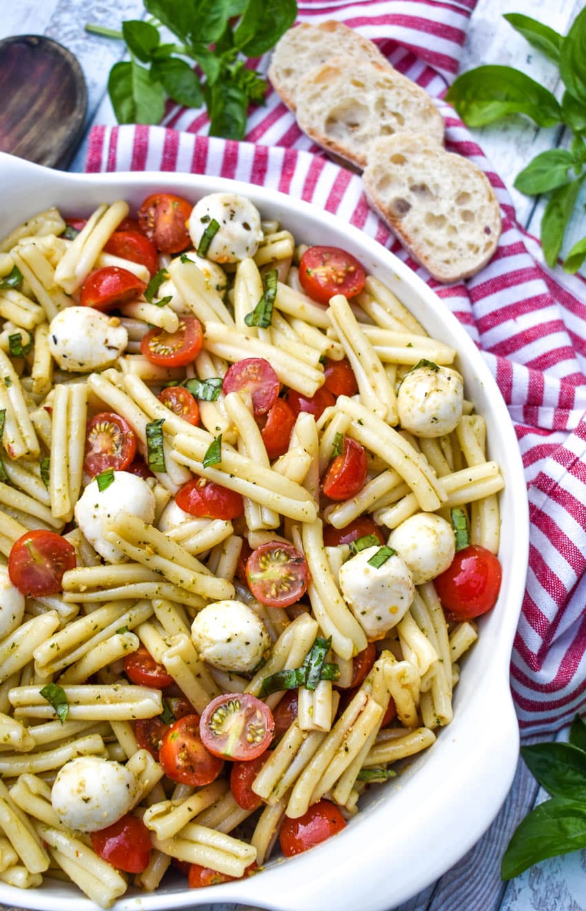 caprese pasta salad in a white serving bowl with a wooden spoon on the side