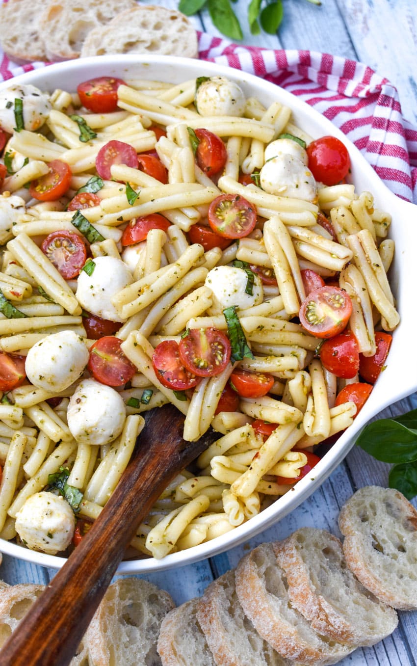 a wooden spoon scooping caprese pasta salad out of a white serving bowl