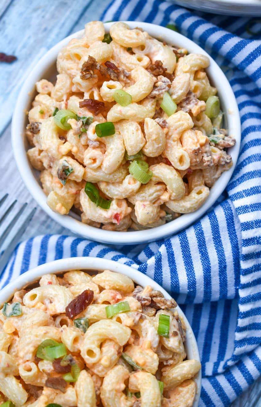 pimento cheese macaroni salad in two small white bowls sitting on a blue and white striped napkin