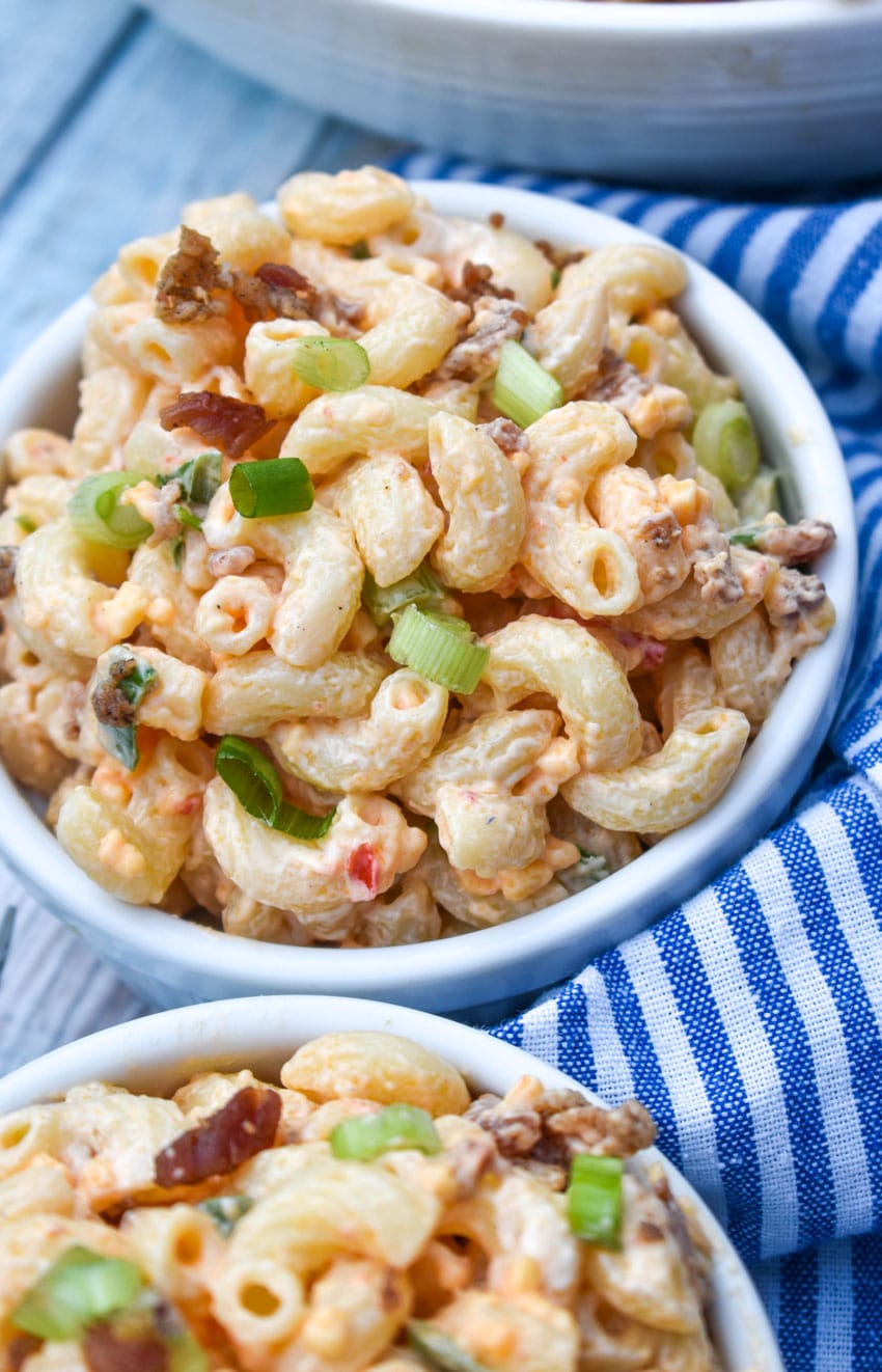 pimento cheese macaroni salad in two small white bowls sitting on a blue and white striped napkin