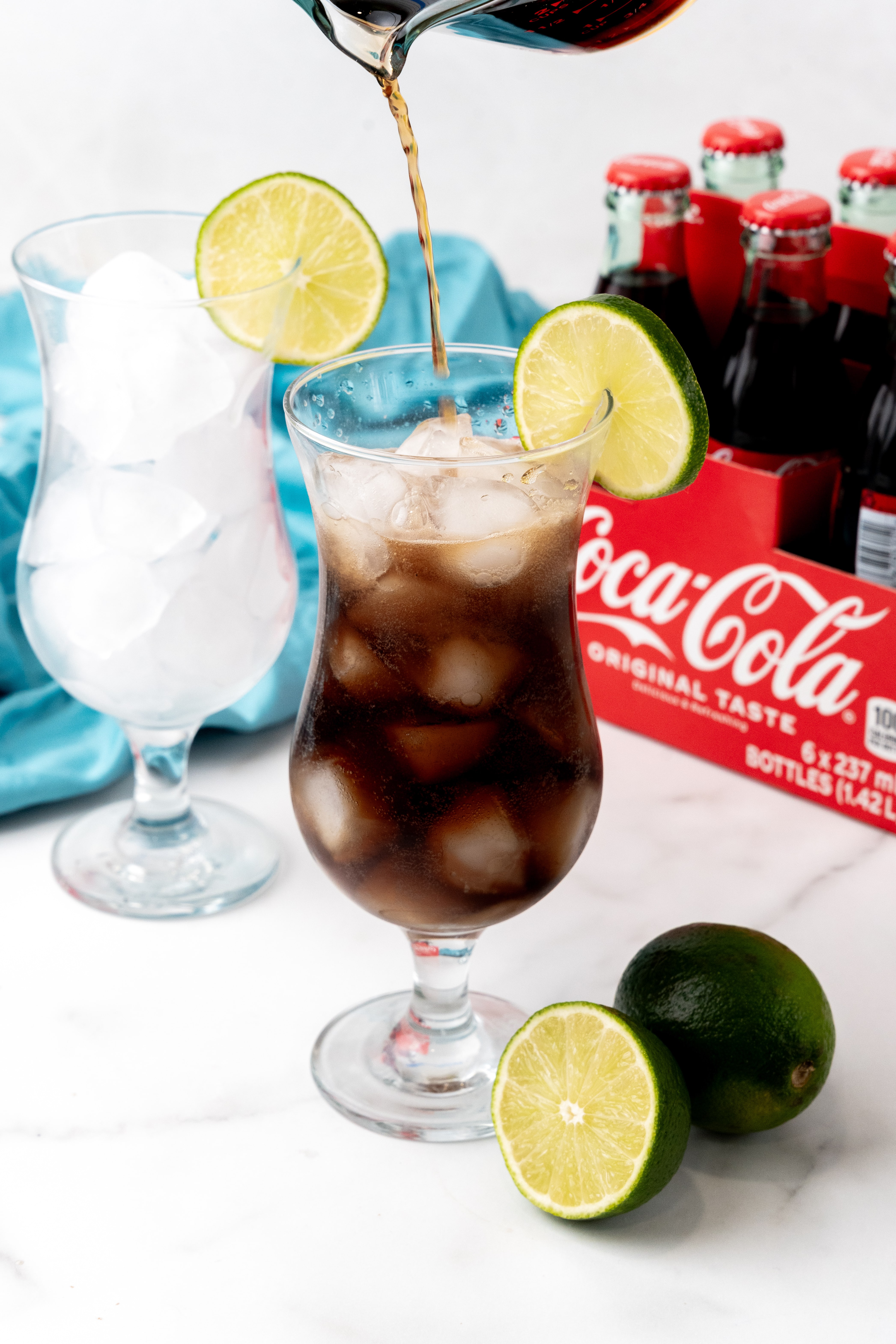 cocoa cola soda being poured over ice in to a drinking glass