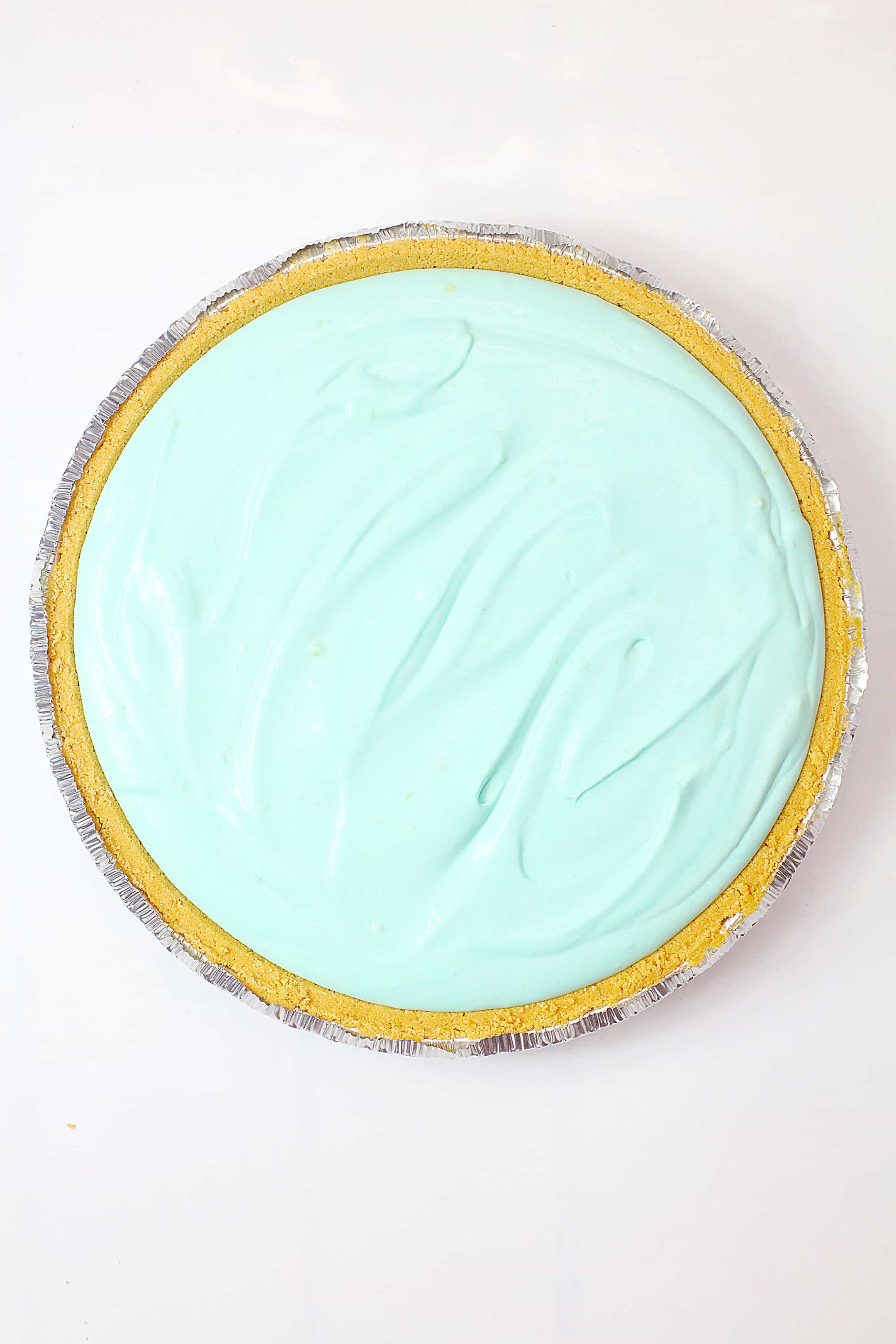 teal dyed pudding spread in a graham cracker crust