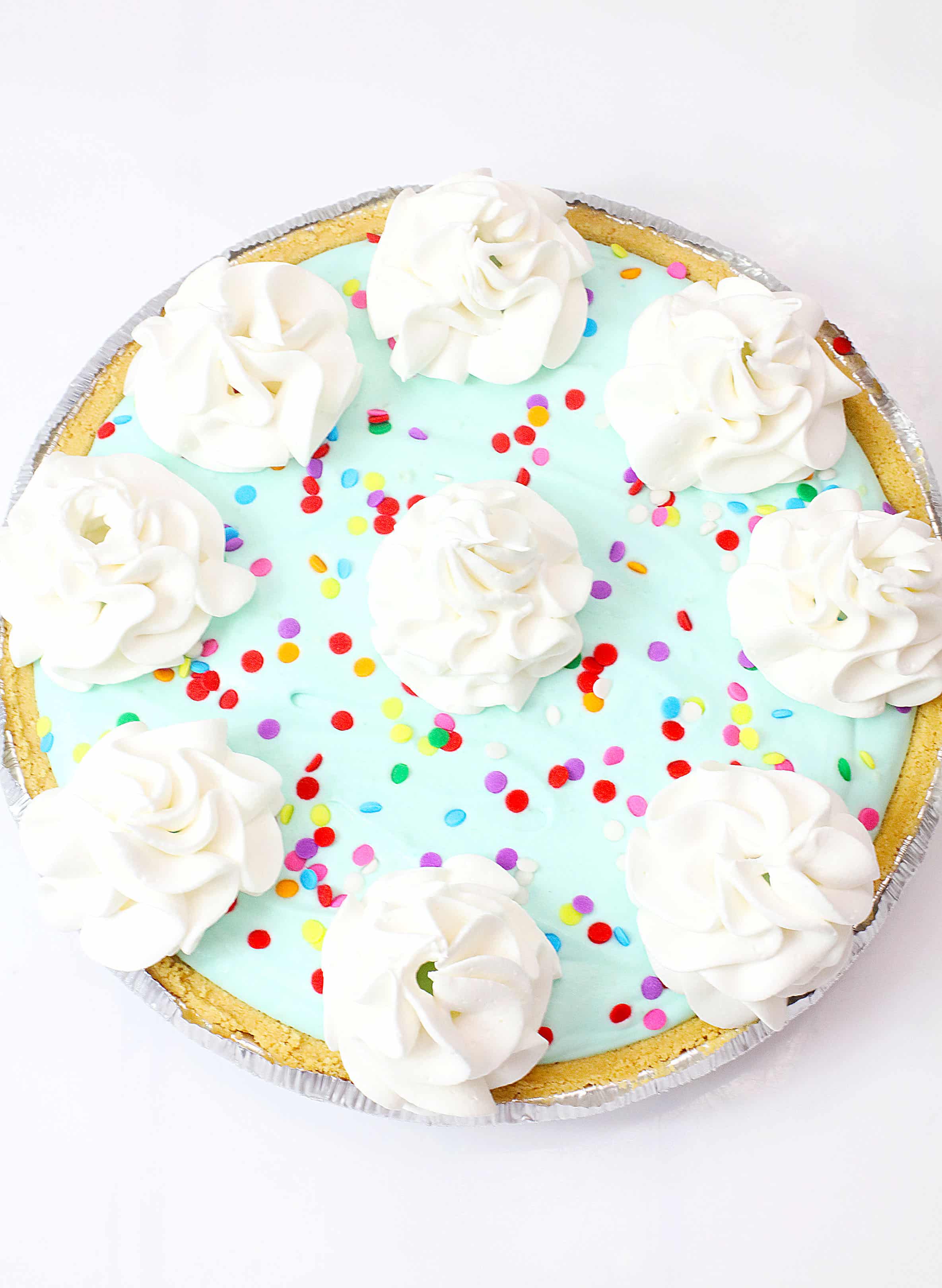 no bake cake batter pie topped with dollops of whipped cream and colorful sprinkles