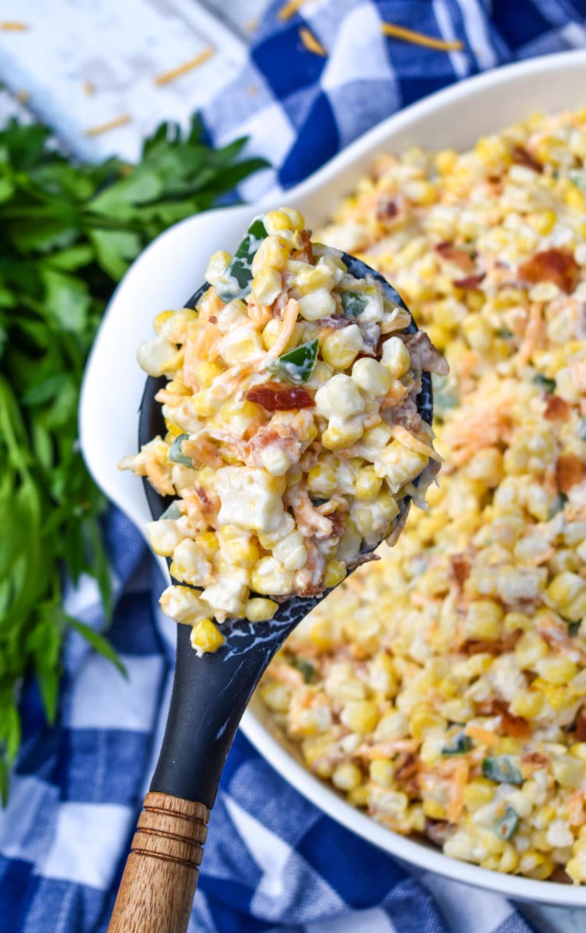 a wooden handled spoon holding up a scoop of jalapeno popper grilled corn salad
