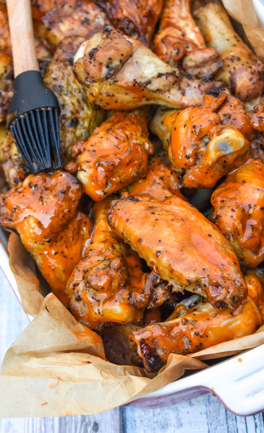 chicken wings in a parchment paper lined baking dish being basted with buffalo sauce