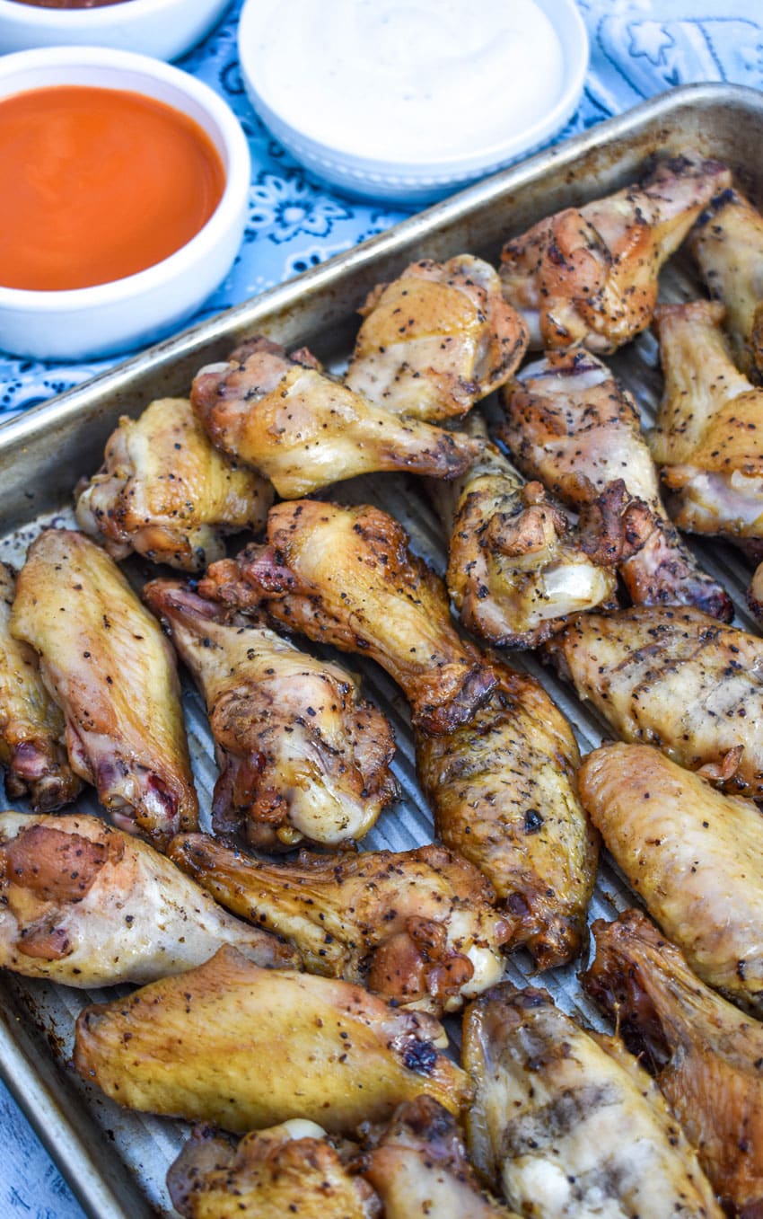 smoked chicken wings on a parchment paper lined baking sheet with assorted dipping bowls of sauces in the background