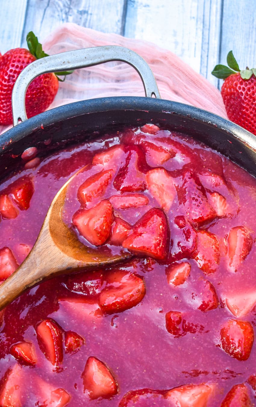 a wooden spoon scooping homemade strawberry pie filling out of a black skillet