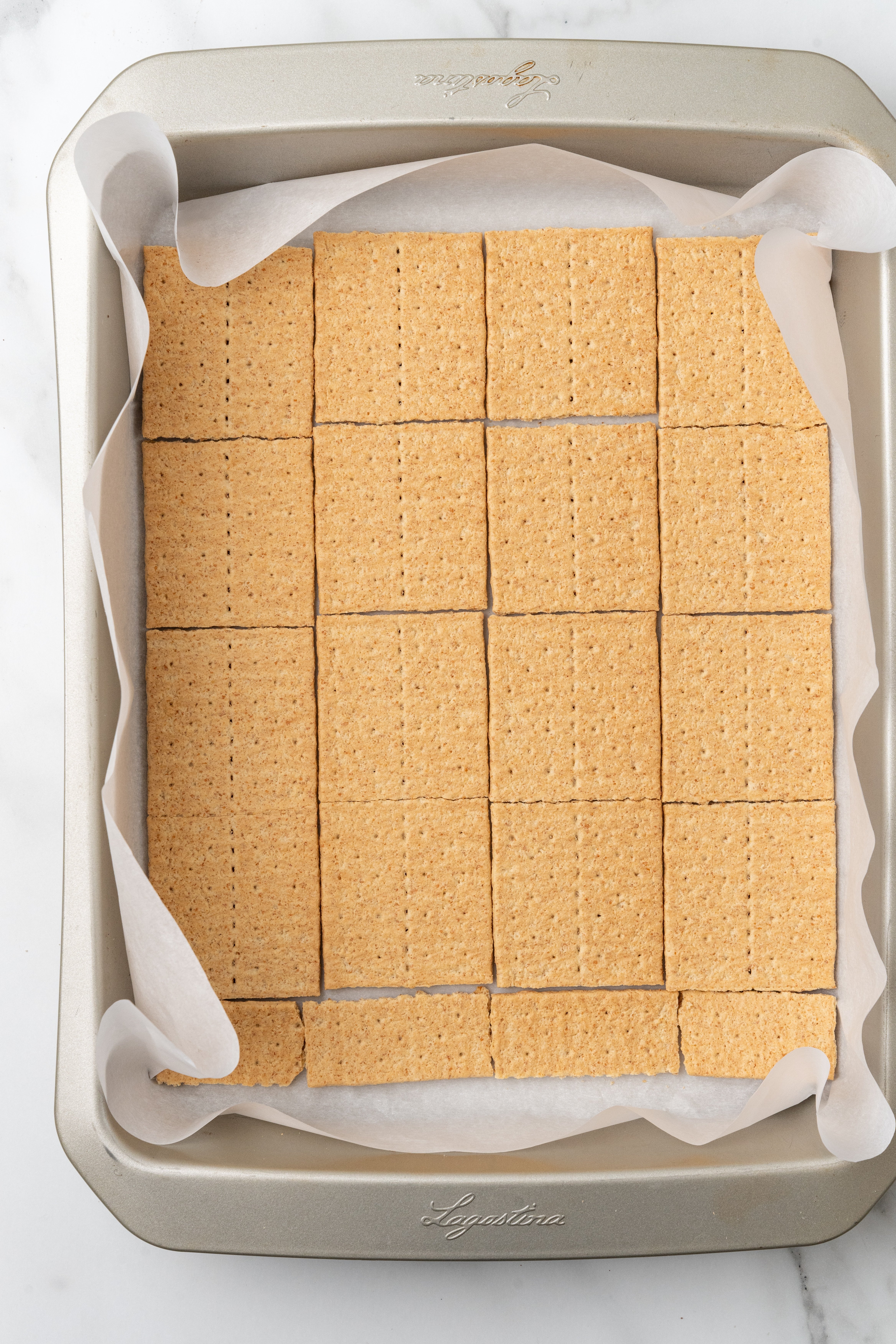 graham cracker squares arranged in the bottom of a parchment paper lined baking pan
