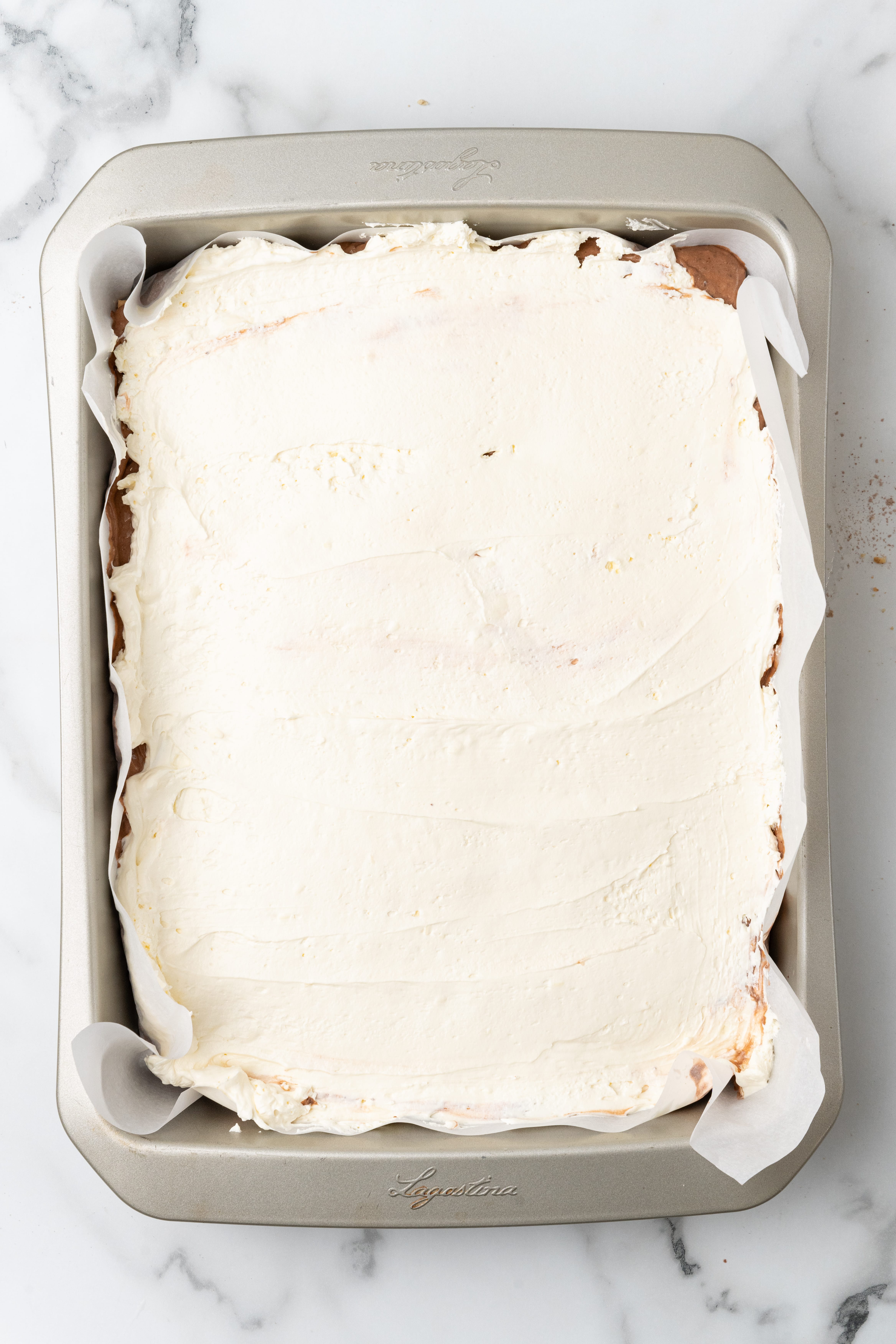 marshmallow fluff spread over chocolate pudding and graham cracker squares in a parchment paper lined baking pan